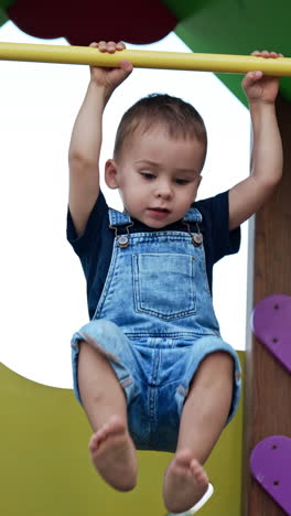 happy smiling caucasian toddler swinging on the horizontal bar. active baby boy sitting on the slide at playground. vertical video