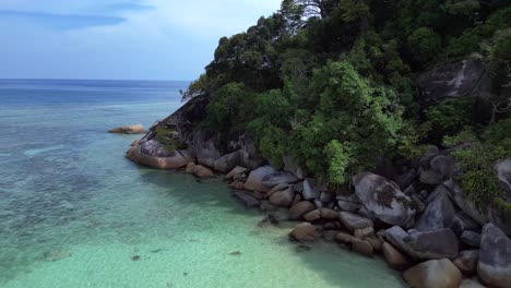 Turquoise-ocean-water-meeting-a-rocky-shore-with-a-lush-green-jungle-forest-on-a-tropical-island