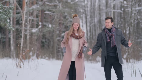 a young man and a woman in a coat are having fun and playing with snow in a winter forest in slow motion. happiness and smiles on faces