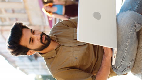 indian man freelancer sitting in city street closes laptop finishing working online distant job