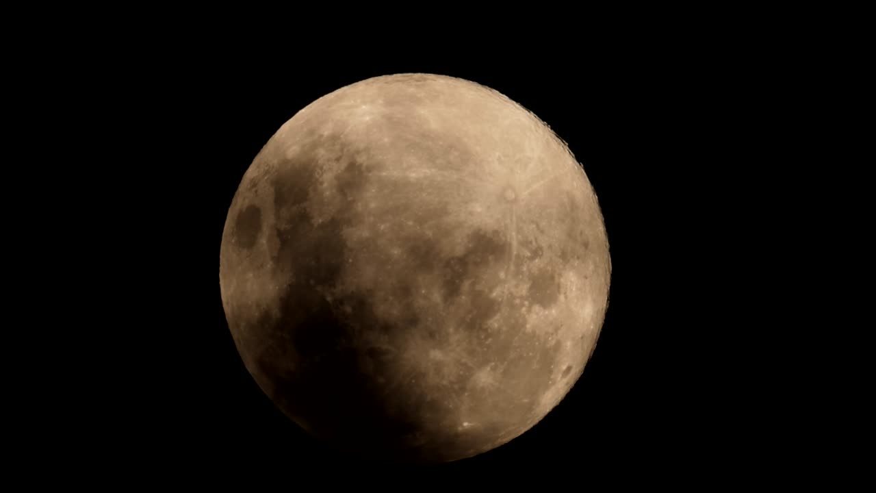 A pink full moon rising from behind dark stormy clouds against a pitch-black night sky