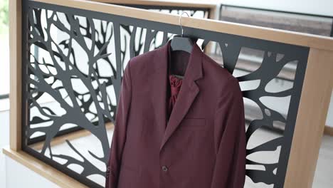 burgundy suit jacket on a hanger, draped over a modern black and wood railing