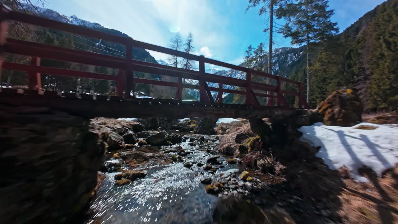 Naturskön träbro över en bäck i snöiga schweiziska Alperna, fridfull och lugn.