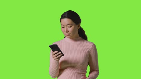 studio shot of woman smiling and laughing at message or content on mobile phone against green screen