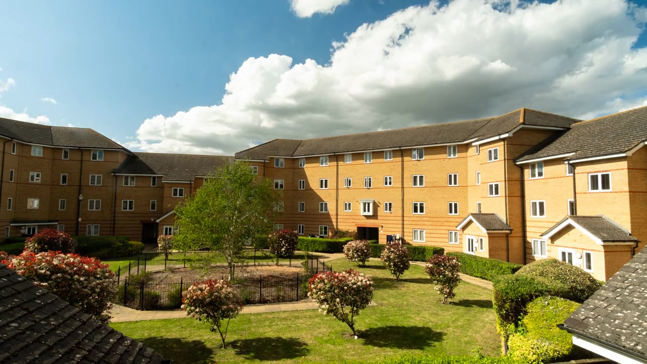 Timelapse of drifting clouds and changing light over a London suburban apartment courtyard and garden.