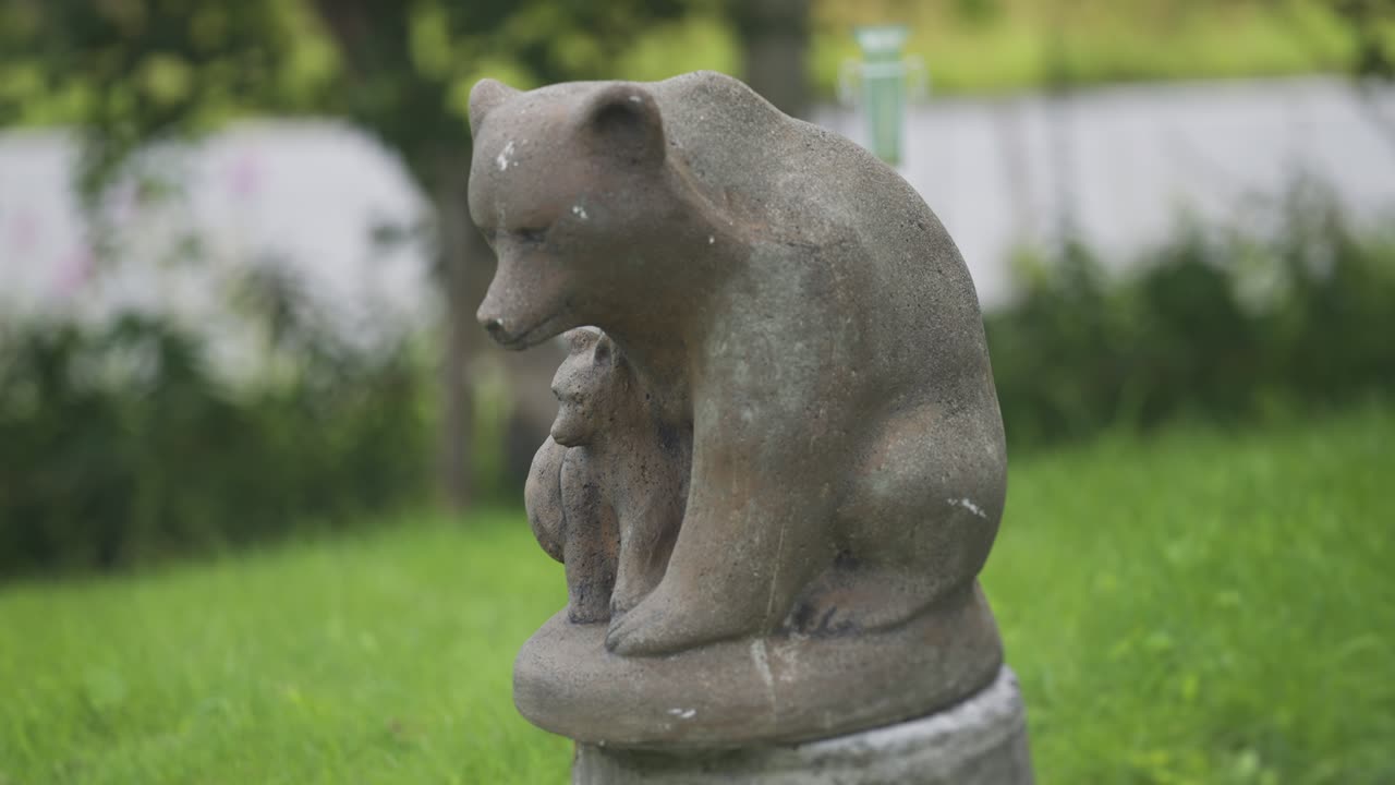 The statue of the mother bear and her cub in the park surrounded by lush grass and trees. A close-up parallax shot.