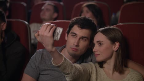 Una-Chica-Haciendo-Selfie-En-Un-Smartphone-Con-Su-Novio-En-El-Cine