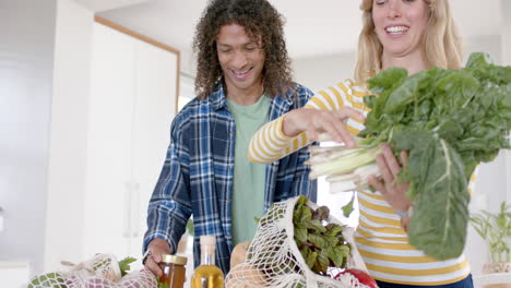 una pareja feliz y diversa desempaquetando bolsas de compras en la cocina, en cámara lenta.