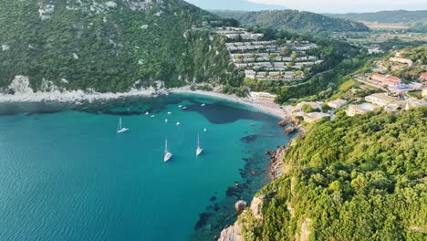 Liapades-beach-on-corfu-island-with-sailboats-and-clear-blue-waters,-lush-greenery-surrounds,-aerial-view