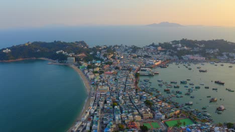 Drone-shot-traveling-upward-above-a-city-built-on-an-isthmus-with-an-harbor-and-a-popular-beach-during-golden-hour