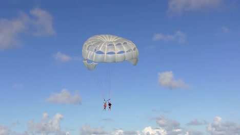 Ein-Paar-Macht-Parasailing,-Auch-Bekannt-Als-Parascending-Oder-Parakiting,-An-Einem-Strahlend-Sonnigen-Tag-Vor-Einem-Blauen-Himmel-Mit-Vereinzelten-Cumulus-Wolken