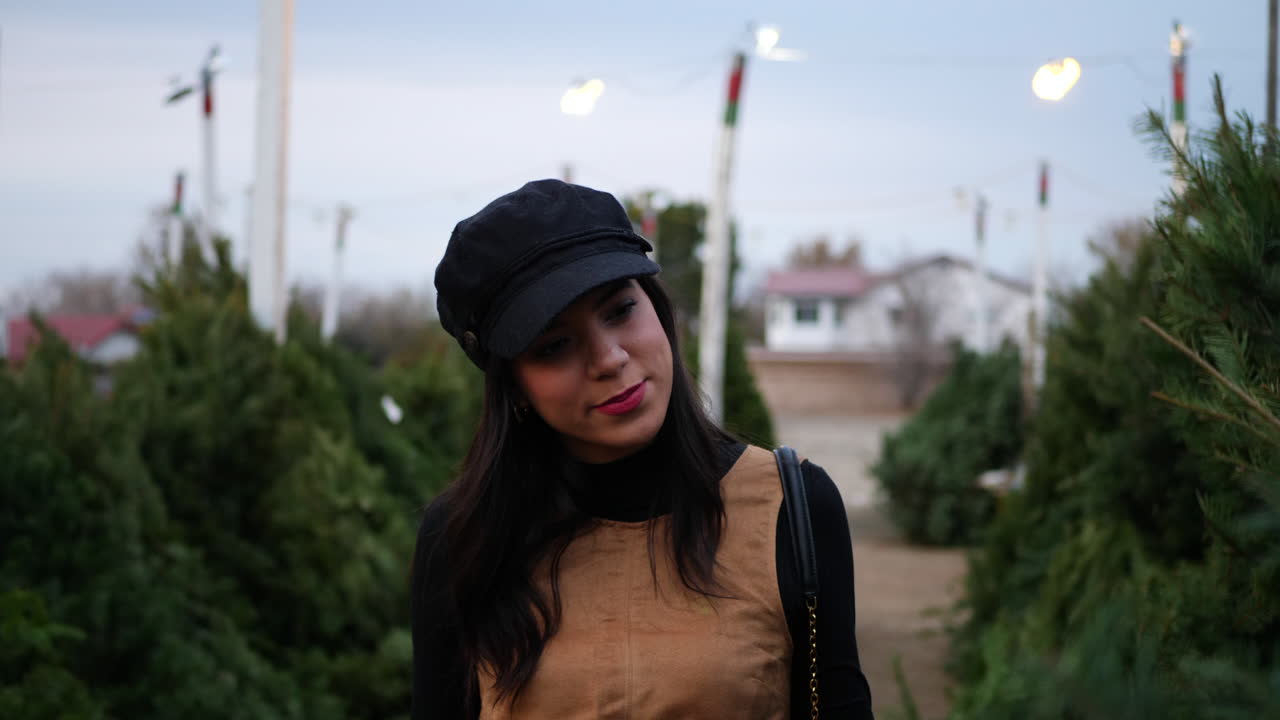 Una donna ispanica che acquista un albero di Natale per le festività in un terreno con molte specie di abeti.