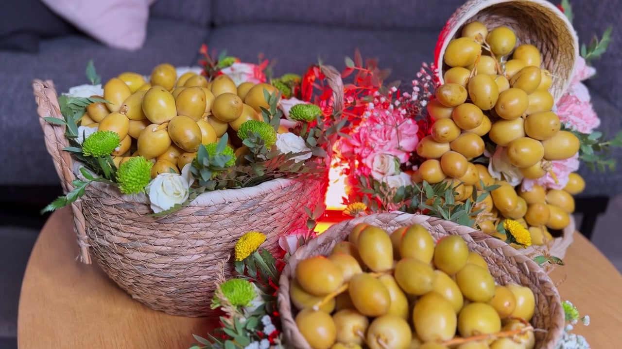 Primo piano di datteri gialli freschi disposti in cesti di vimini intrecciati decorati con fiori freschi. L'esposizione del dolce raccolto agricolo è su un tavolo di legno all'interno con una profondità di campo ridotta