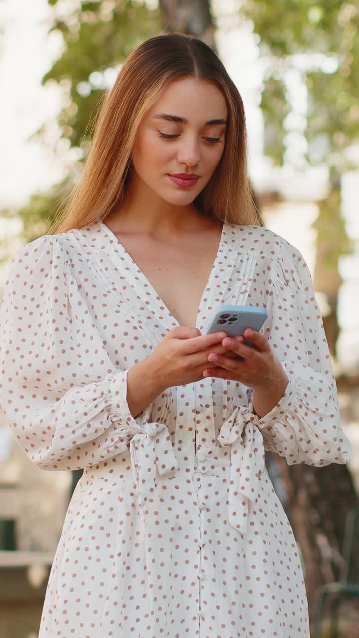 Giovane donna caucasica che usa lo smartphone, scrive messaggi sui social media, invia e-mail in una strada della città.