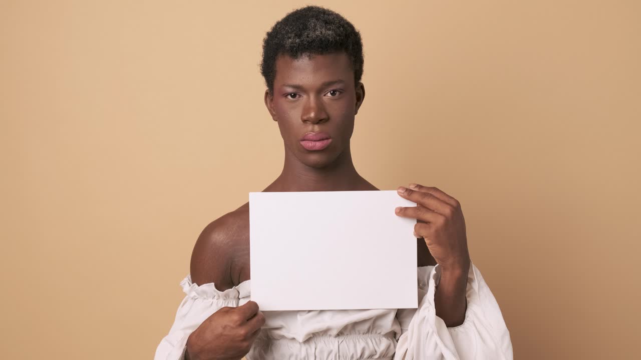 Transgender person with serious face holding a white blank paper sheet over an isolated background.