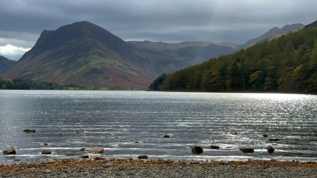 Timelapse on the shore of Buttermere Lake with sun rays shining through the clouds, mountains and trees - Lake District