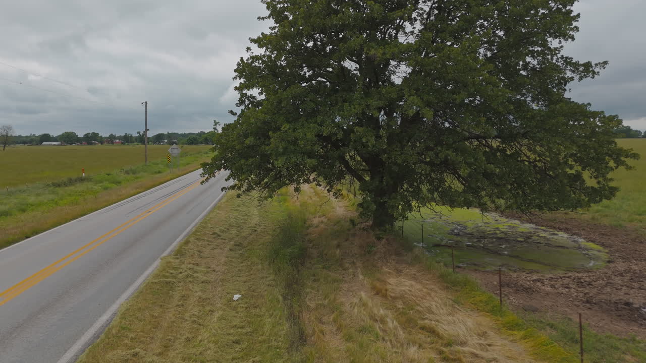 Rural road sign for Colcord OK West 12 with trees and fields on both sides near Cherokee City, Arkansas, aerial pullback as cars pass in slow motion