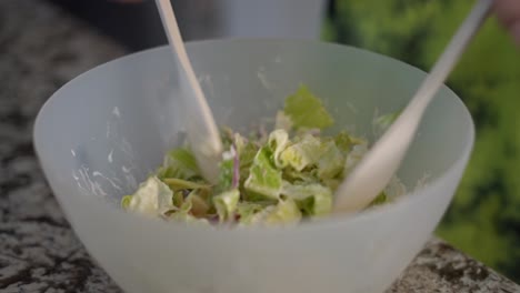 mixing healthy salad in large bowl with greens using two salad spoons, close up