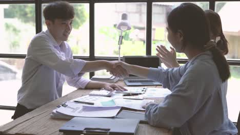 young asian business people shaking hands in the office. finishing successful meeting. three persons.