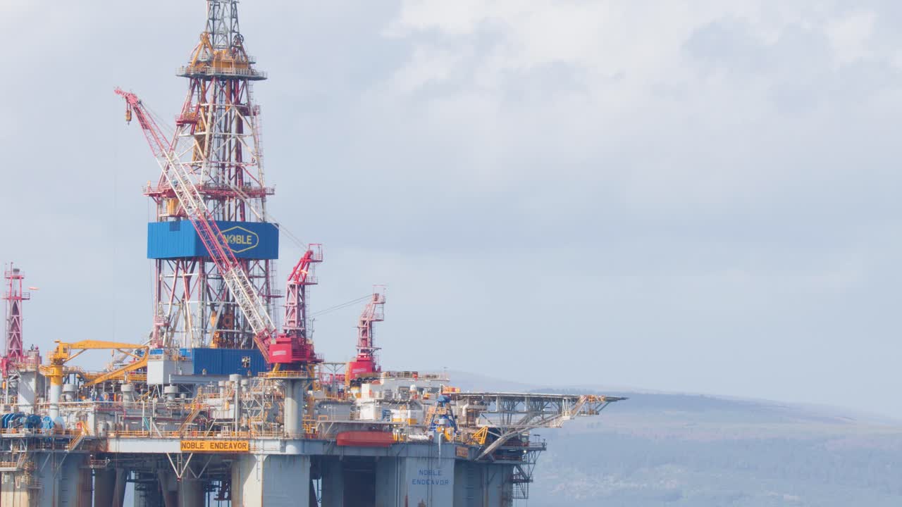 Stor offshore olieplatform i Nordsøen, kameraet panorerer langsomt, klart dagslys, fjerne bakker