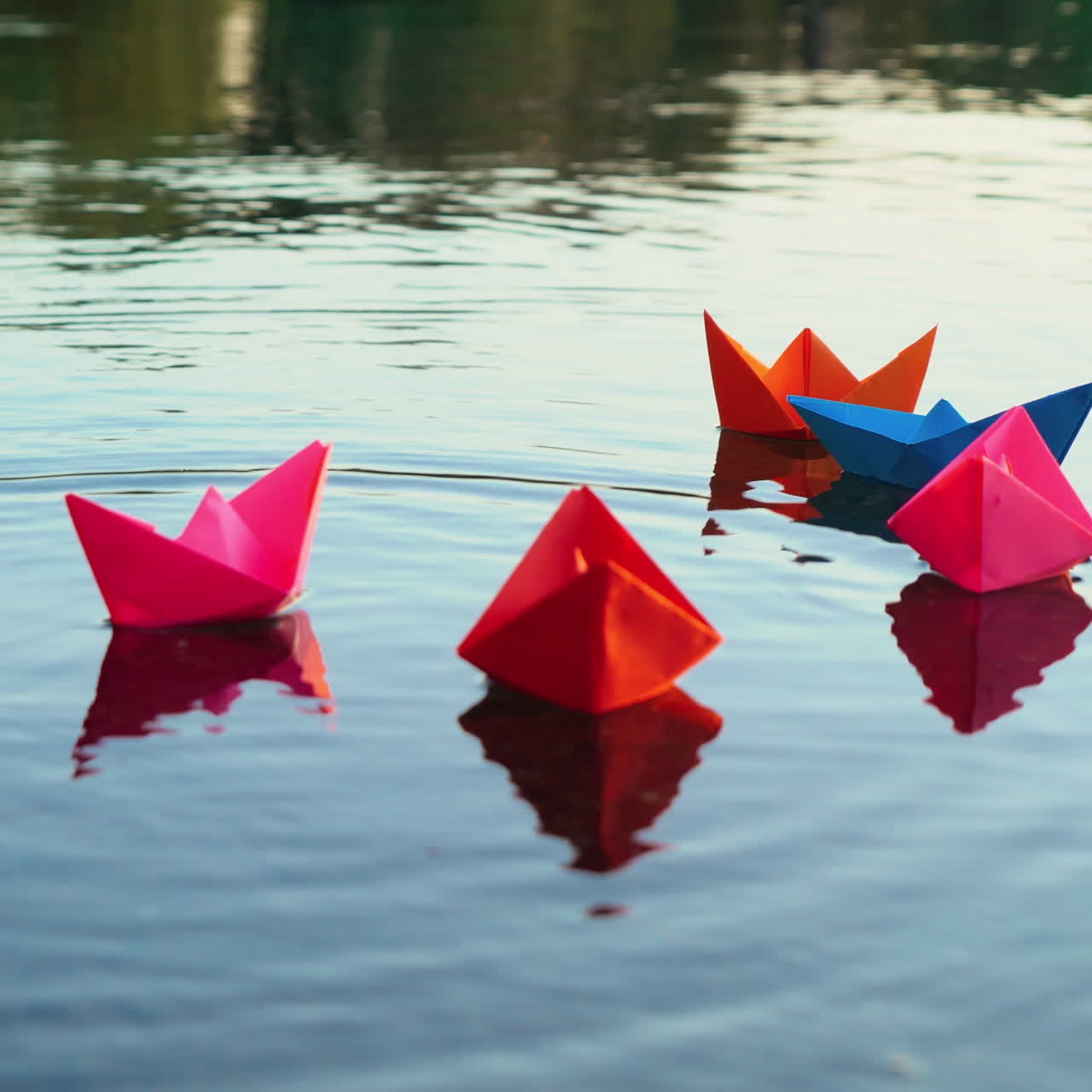 Woman's hand is putting coloured paper ships into the water in the evening. Bright origami boats in the river surface. Origami ship sailing.