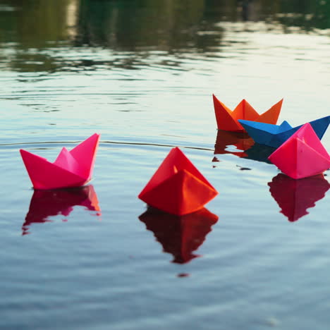 vrouwelijke hand zet gekleurde papieren schepen in het water in de avond. heldere origami boten in het rivieroppervlak. origami schip zeilen.