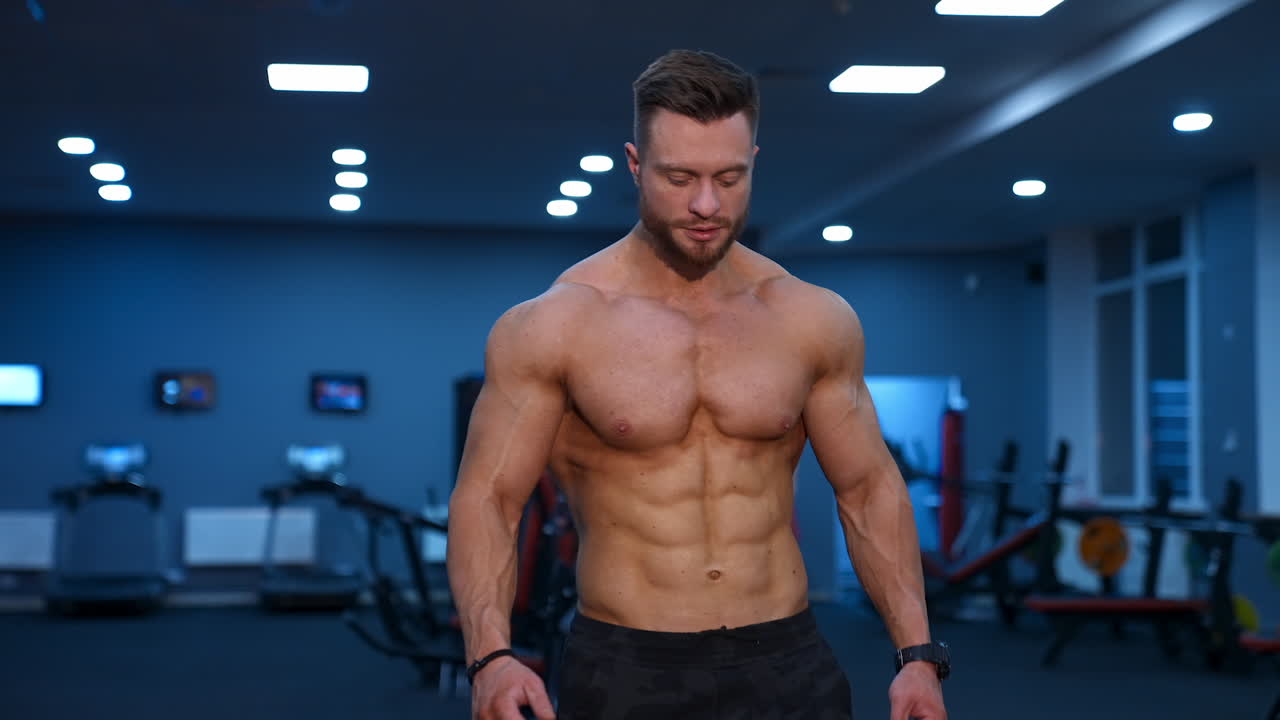 Muscle athlete strongman walks in a gym after heavy training. Perfect torso with strong abs. Handsome power male with naked torso.