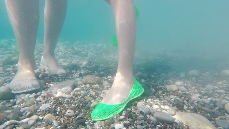 Gambe con scarpe protettive sul fondo ciottoloso del mare: concetto di bagno sicuro