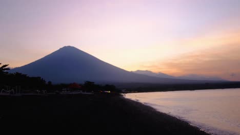 silhouetted mt agung volcano during stunning golden pink sky sunset reflecting on ocean in amed on tropical island of bali indonesia