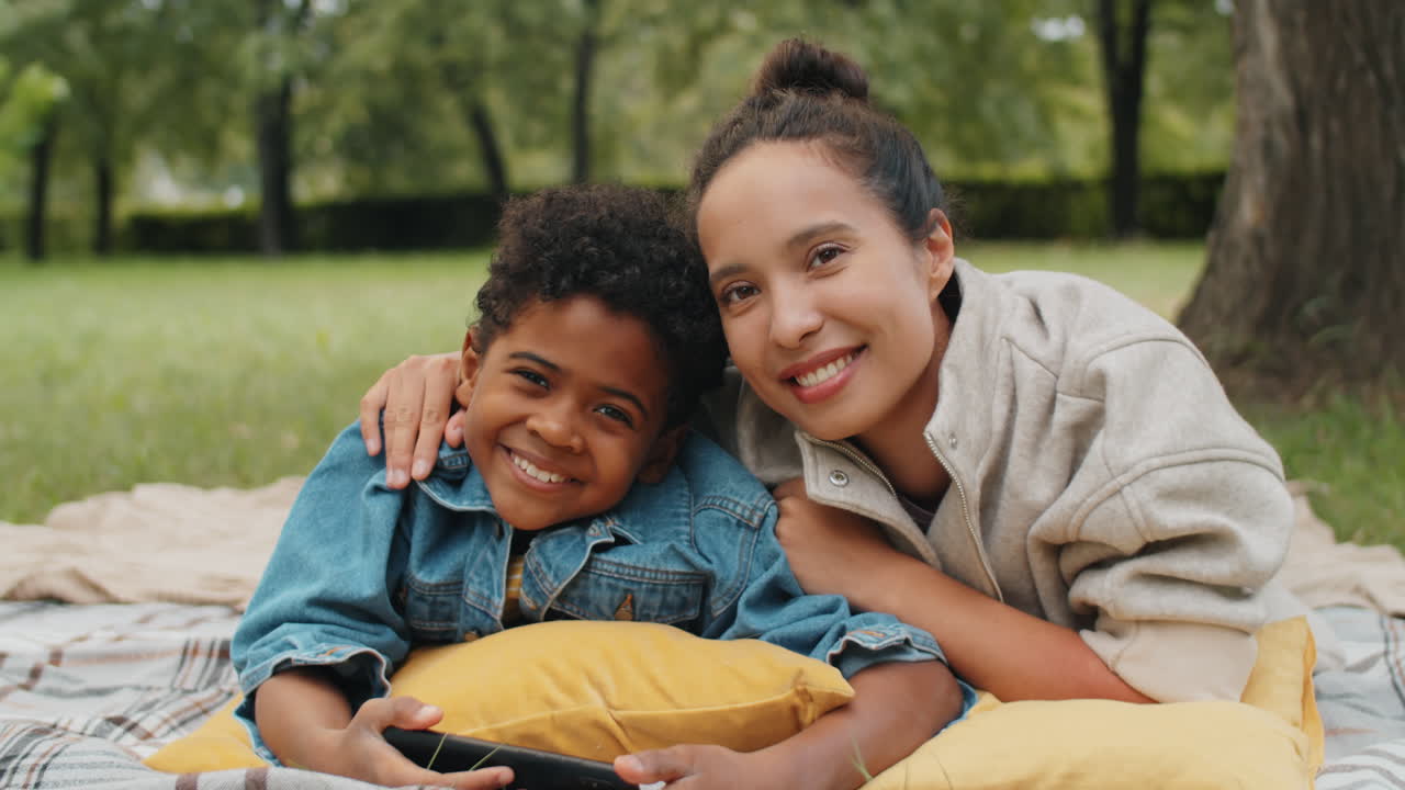 retrato de una madre y un hijo afroamericanos sonrientes acostados en un parque