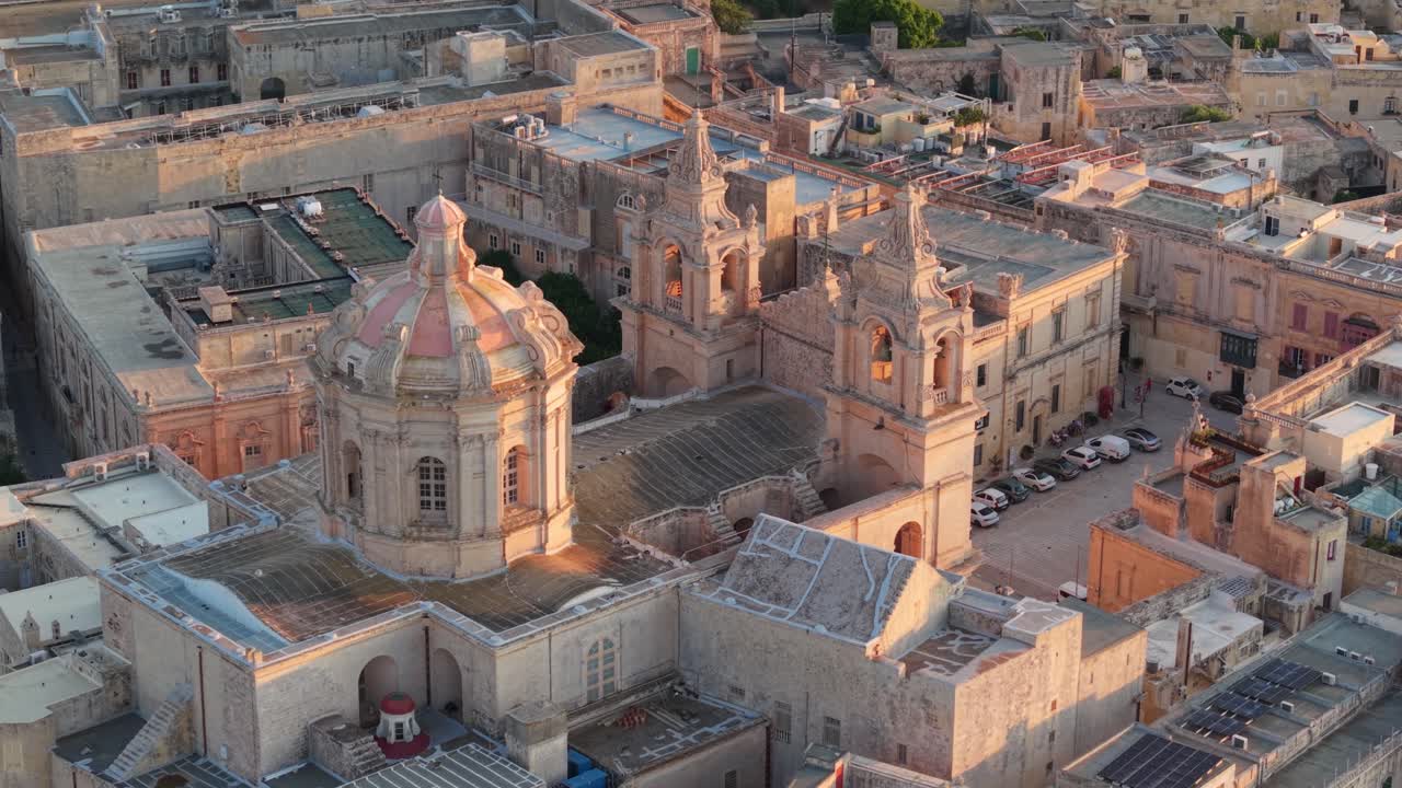 A detailed aerial view of St. Paul's Cathedral in Mdina, Malta, showcasing its baroque dome, twin bell towers, and intricate stonework