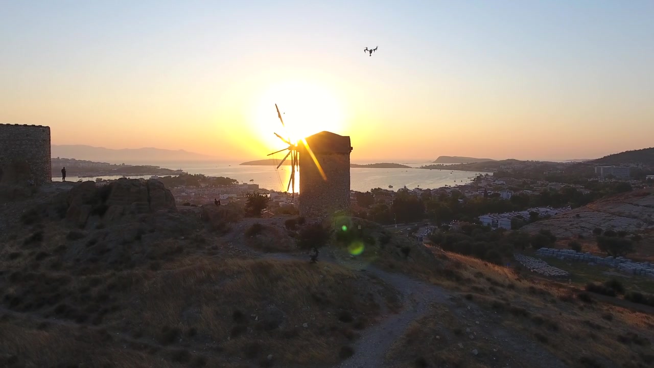 Vista aérea de moinho de vento histórico ao pôr do sol com vista para uma cidade costeira