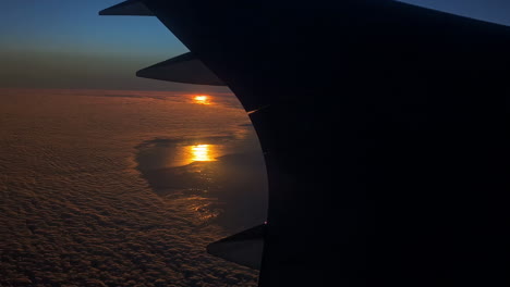 stunning footage of white clouds below from airplane window with sun setting in the background along blue sky