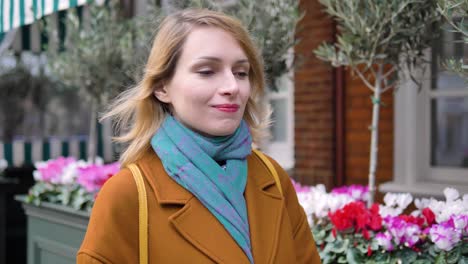 Happy-cheerful-positive-and-relaxed-young-Caucasian-woman-enjoying-her-walk-down-a-London-street-full-of-flowers,-and-looking-around