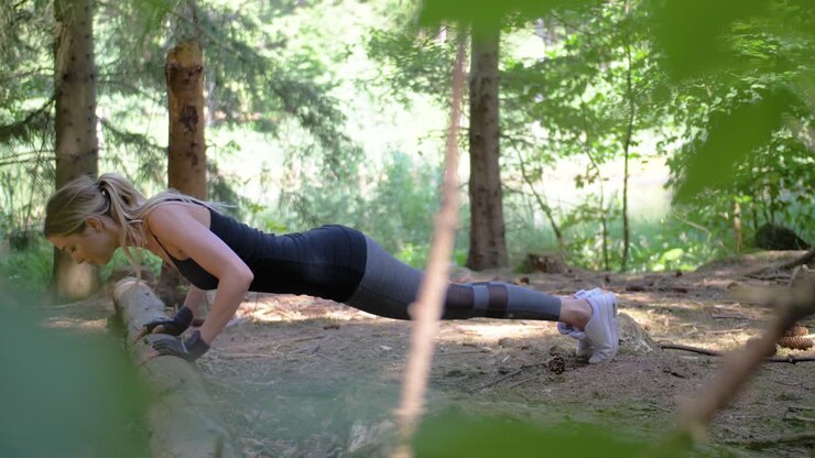 A thin, fit, young woman exercising by doing push-ups in a wooded setting
