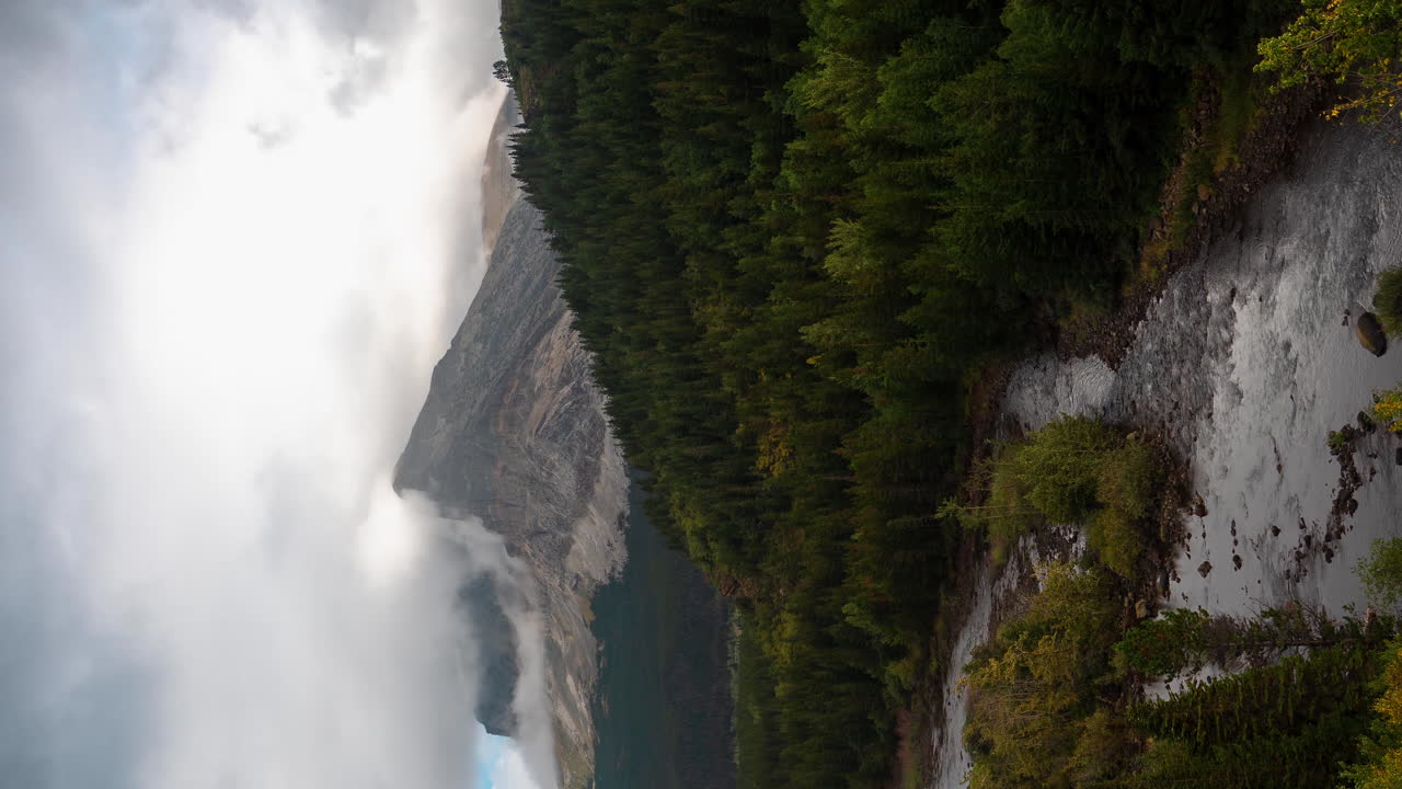 lapso de tiempo vertical de 4k, nubes dramáticas sobre majestuosas montañas vírgenes paisaje bosque, río glacial y picos