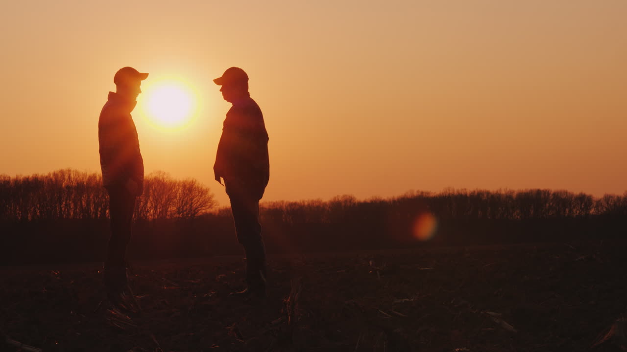 dos granjeros se dan la mano en un campo al atardecer