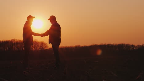 Zwei-Bauern-Schütteln-Sich-Die-Hände,-Die-Bei-Sonnenuntergang-Auf-Einem-Feld-Stehen
