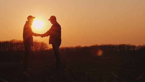 dos granjeros se dan la mano en un campo al atardecer