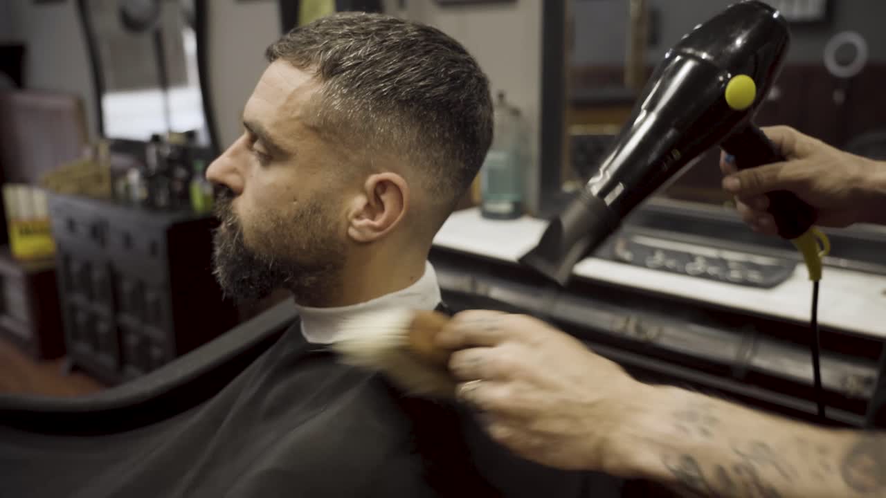 Barber bruger hårtørrer og børste til at afslutte hårstylingen – nærbillede.