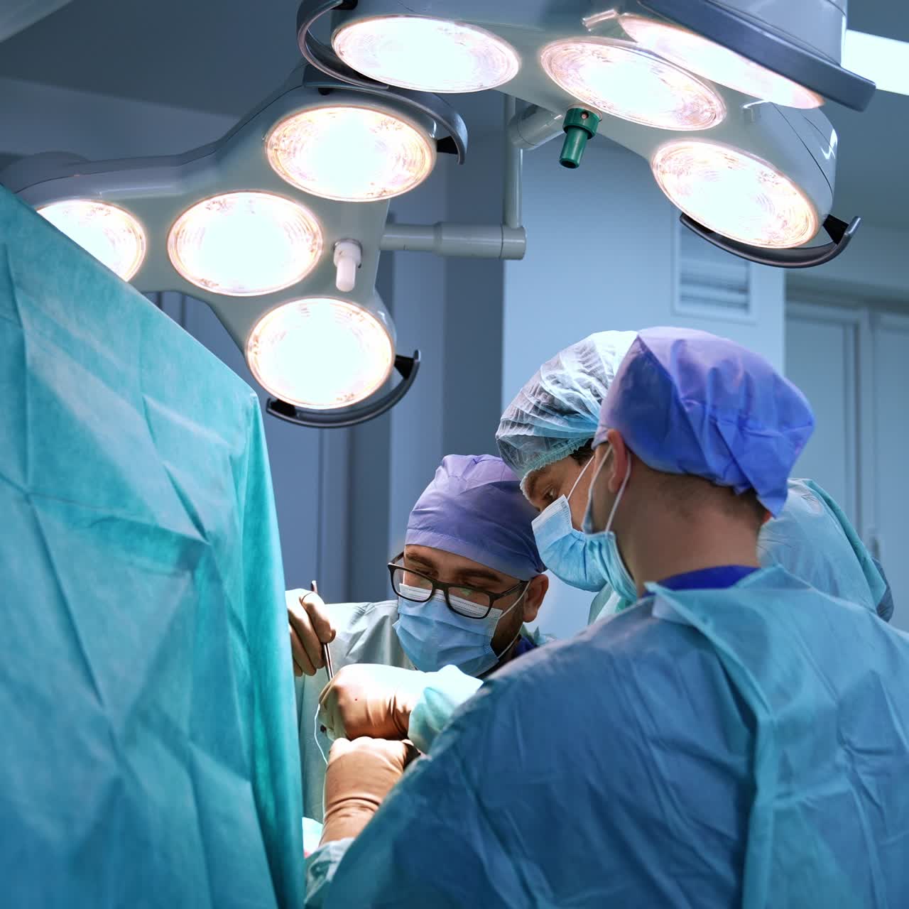 Professional surgeons performing operation in the surgical room. Doctors work under bright lamps at operational theatre