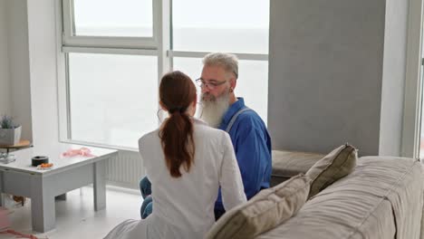 A-brunette-girl-with-a-stethoscope-a-doctor-in-a-medical-gown-examines-a-man-and-listens-to-his-heartbeat-during-a-home-examination.-An-elderly-man-with-gray-hair-and-a-thick-beard-conducts-a-home-examination-with-a-doctor