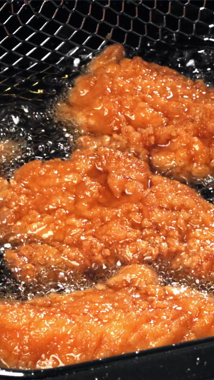 熱い油で揚がるきつね色のフライドチキンのクローズアップ