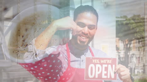acercamiento de una taza de café contra un camarero afroamericano que sostiene un cartel abierto fuera del café