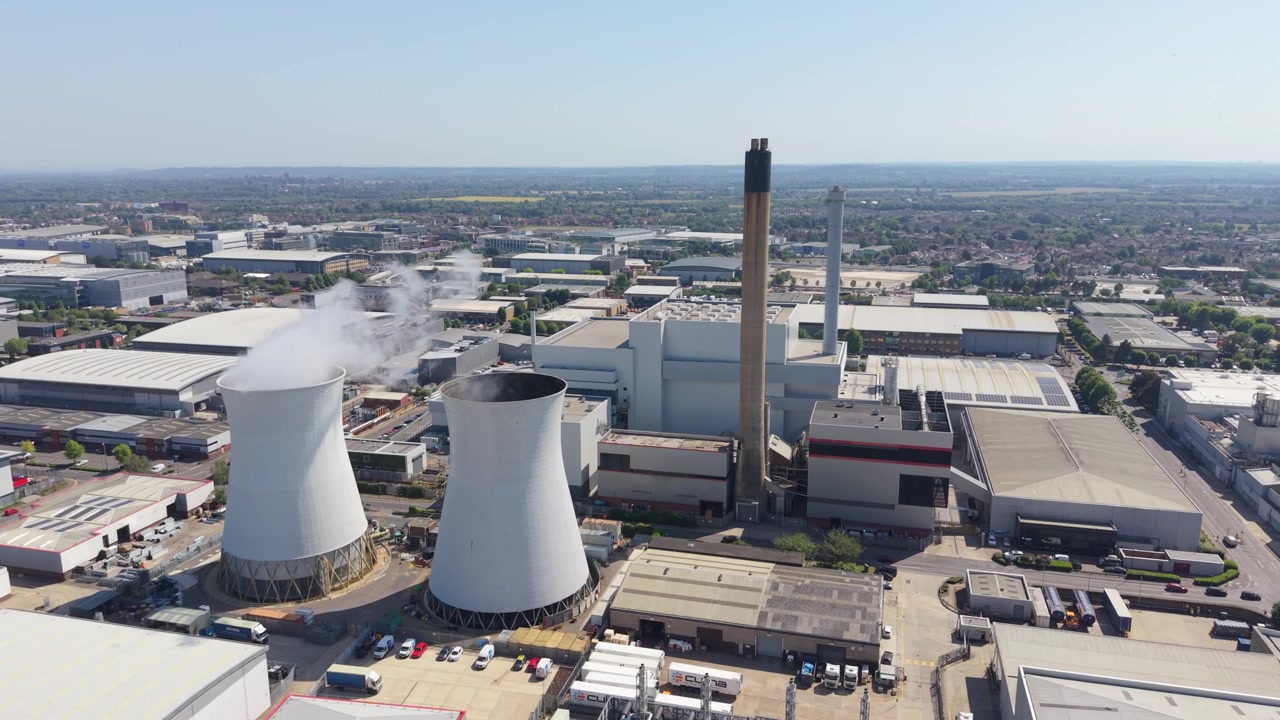 Vista aerea di una centrale elettrica multi-combustibile che genera energia dai rifiuti. Grandi torri di raffreddamento emettono vapore in una giornata limpida e soleggiata. Questo complesso industriale si trova in un'area urbana.