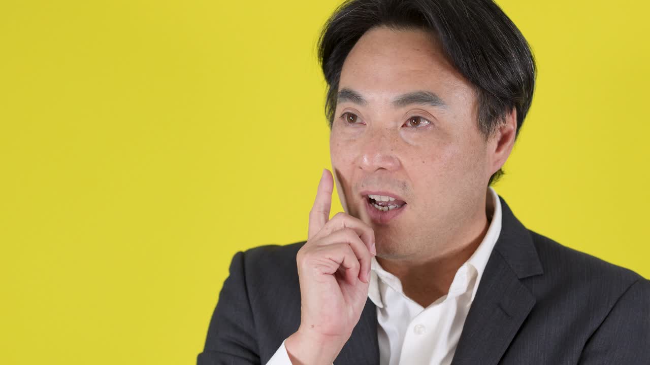 정장을 입은 남자가 생각하는 모습에서 영감을 받아 의기양양해하는 모습으로 바뀌는 장면, 밝은 조명, 고정 카메라