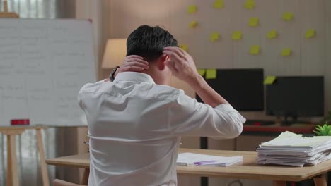 vista trasera de un hombre asiático estirándose después de trabajar duro con documentos en la oficina