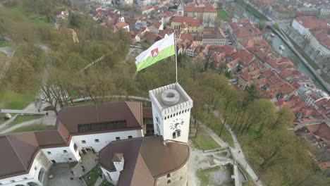 Fly-over-Ljubljana-castle-and-flag,-one-of-the-most-important-landmarks-of-the-city,-Slovenia