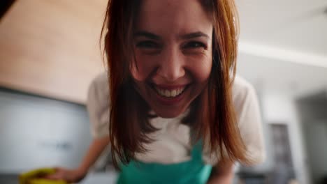 Portrait-of-a-happy-and-cheerful-brunette-cleaning-lady-girl-in-a-white-T-shirt-holding-a-window-and-looking-out-of-it-while-cleaning-in-a-modern-kitchen