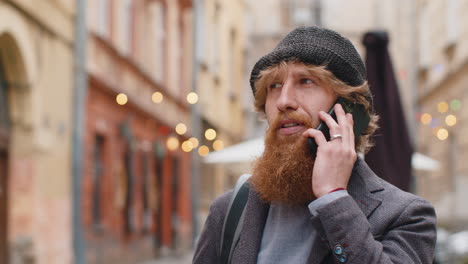 a man with a red beard talking on the phone on a city street